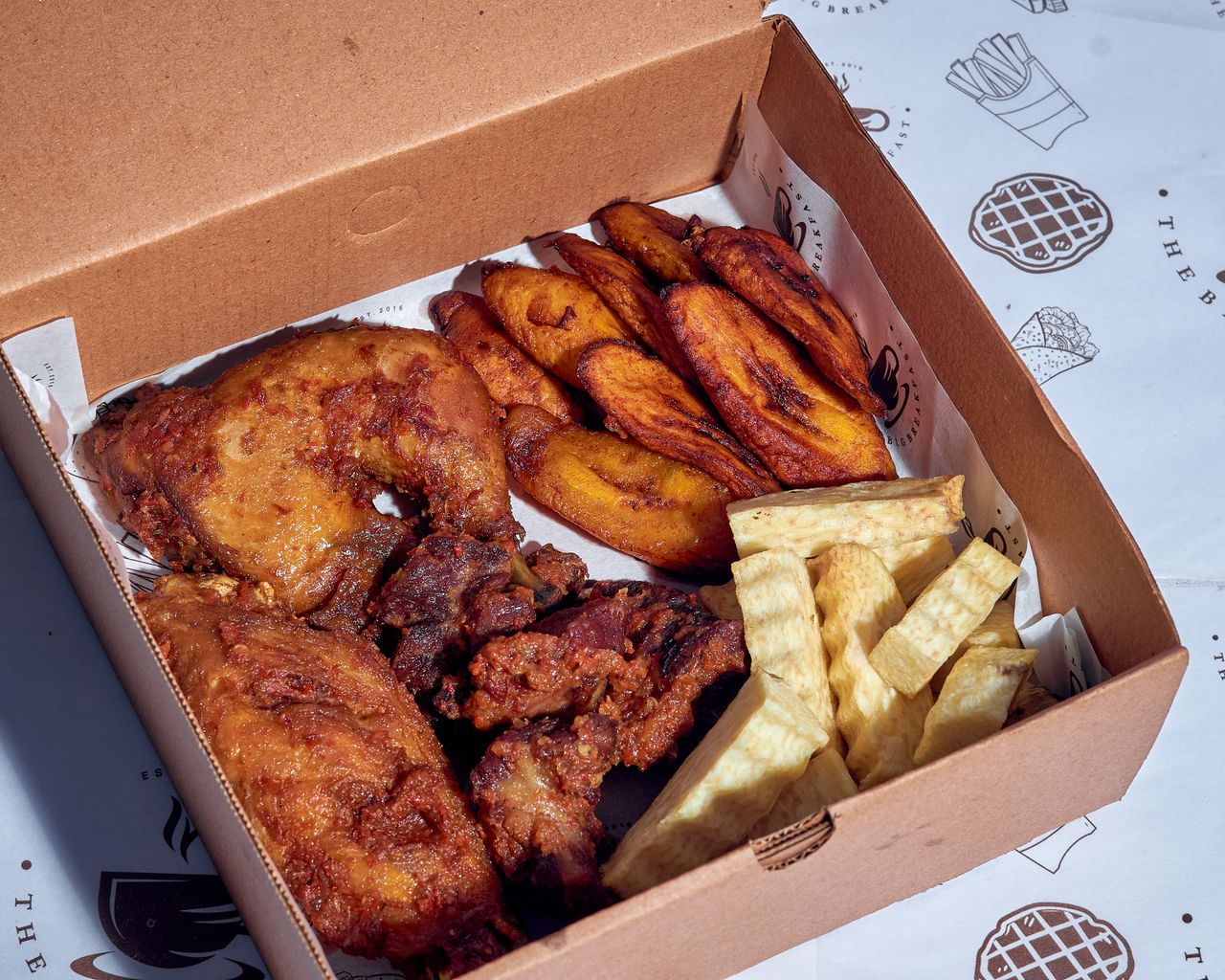 Accueil Crispy fried chicken with plantains and fries in a cardboard takeout box, ideal for food photography.