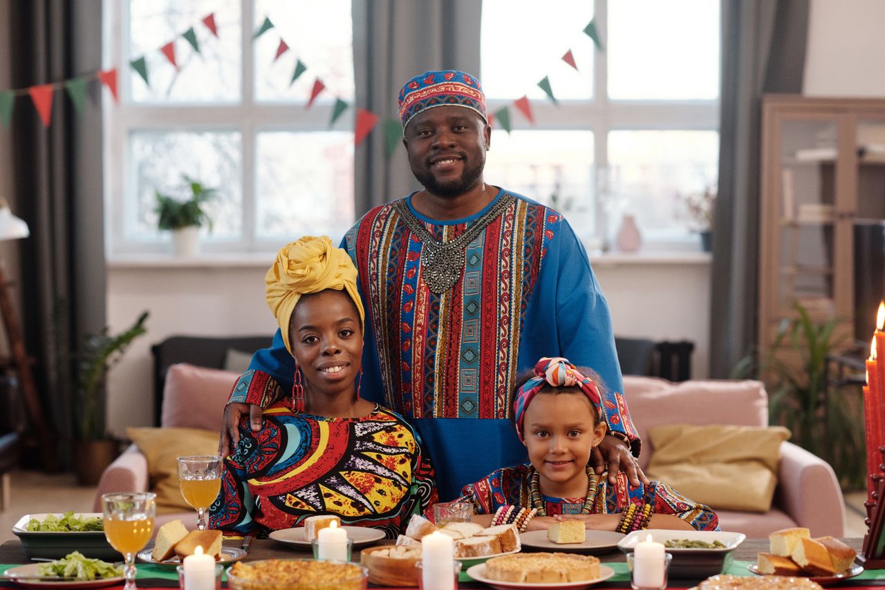 A joyful family in traditional attire celebrates Kwanzaa around a festive dinner table.