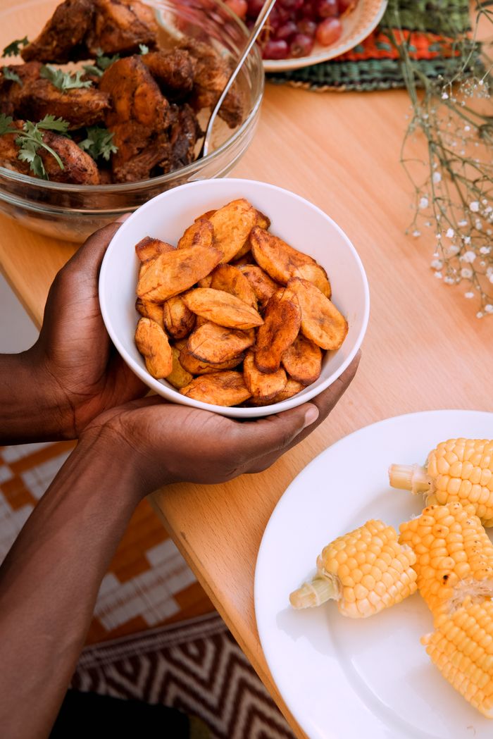 Accueil A vibrant African meal featuring fried plantains, chicken, and corn on a wooden table.